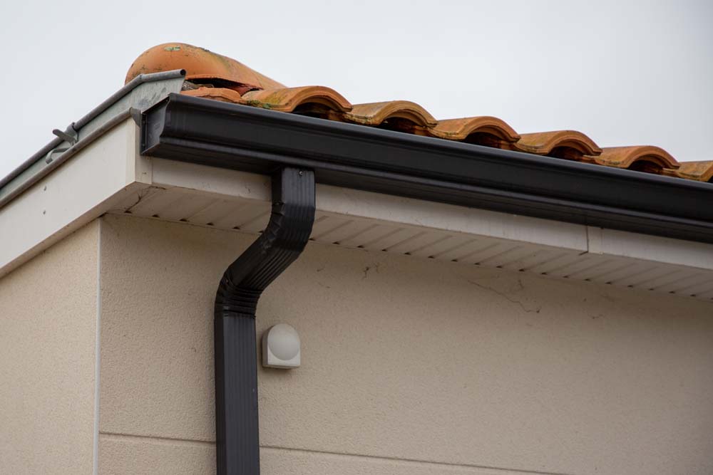 metal black gutter on home roof covered with ceramic tiles Close up